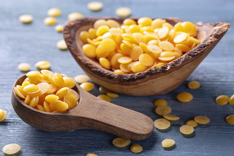 Yellow lentils in a wooden scoop and bowl on a blue surface
