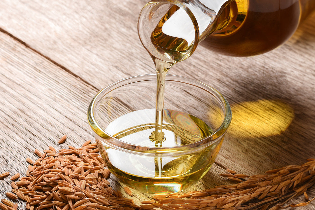 Oil being poured into a glass bowl with seeds on a wooden surface