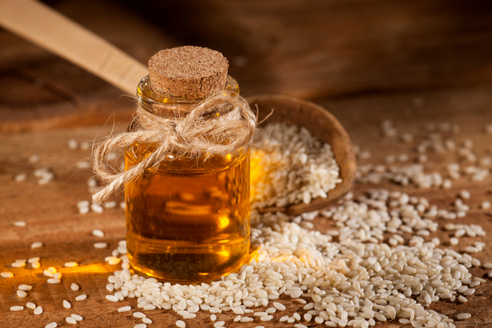 Small bottle of oil with a cork lid on a wooden surface with sesame seeds