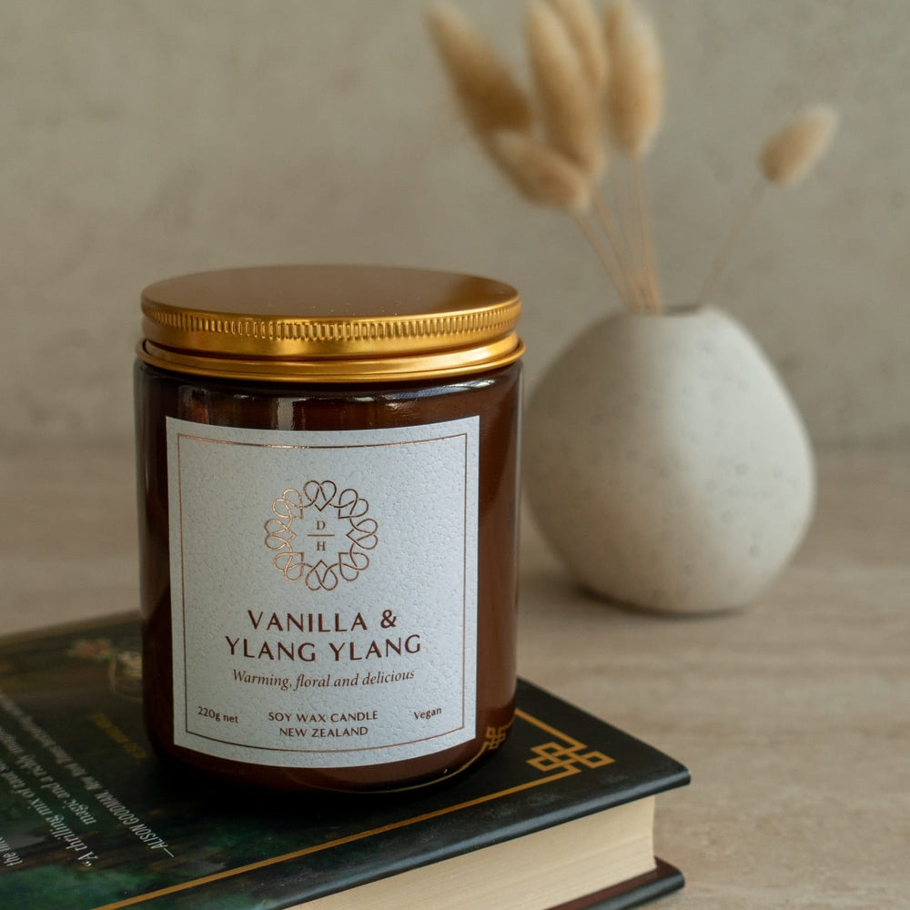 Vanilla & Ylang Ylang candle jar on a book with a vase in the background made in nz