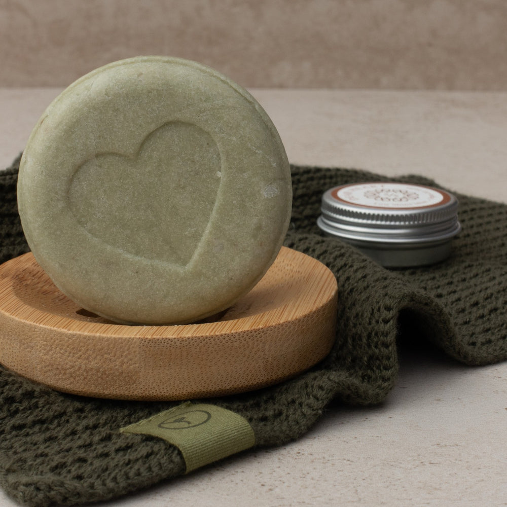 close up photo of shampoo bar on a bamboo rack with washcloth and lip balm in a tin