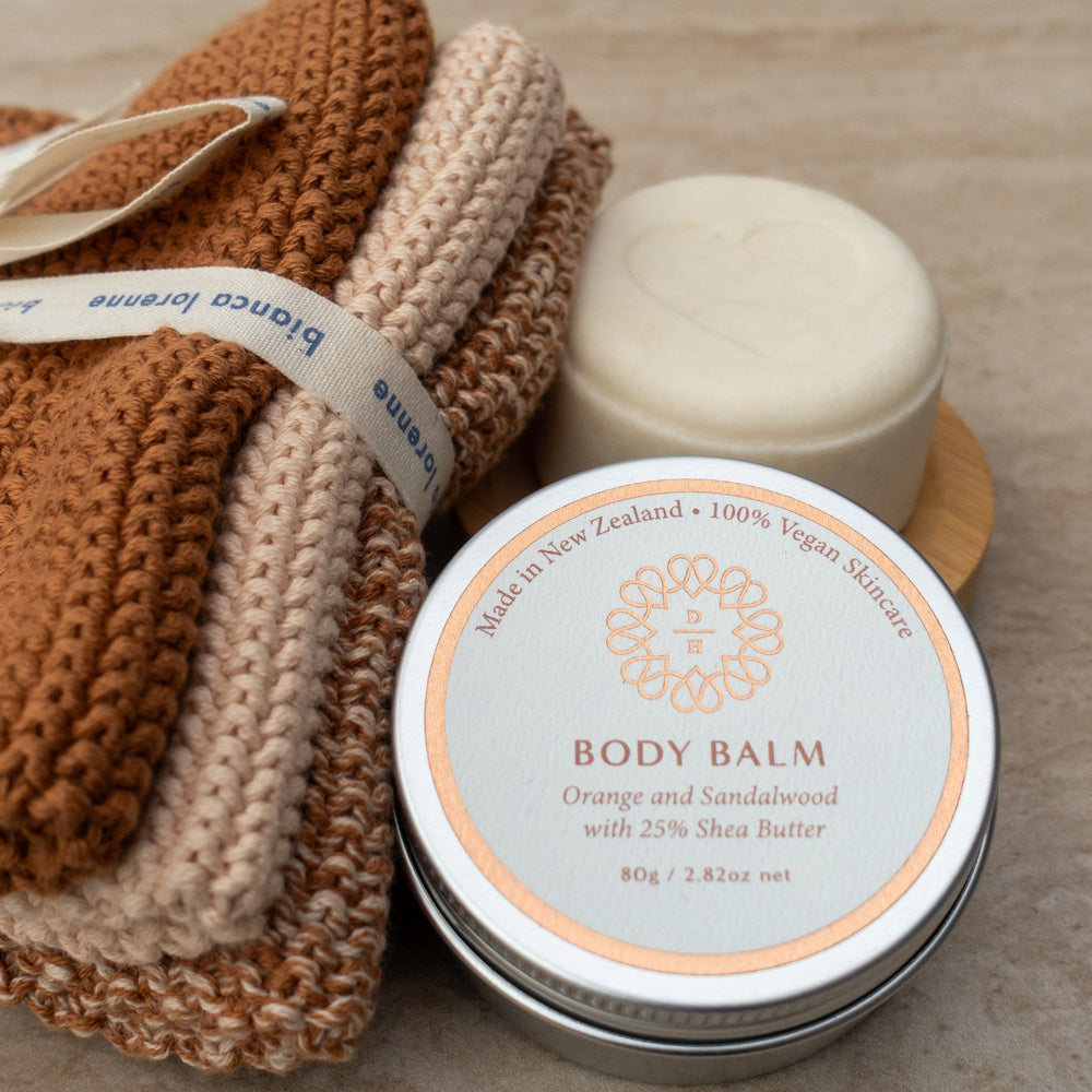 closeup photo of washcloth trio showing knitted detailing, creamy oats bar on a dish with the body balm 