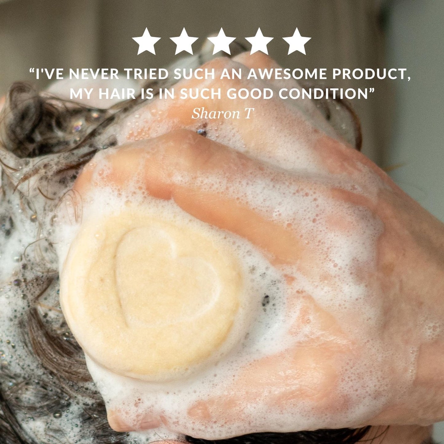 A close-up of a hand washing hair with a lathering shampoo bar indian summer type, overlaid with a five-star review quote from a customer I've never tried such an awesome product, my hair is in such good condition